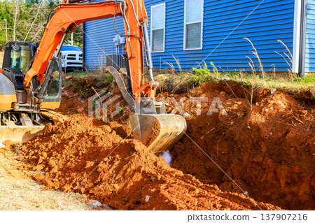 Excavator digs trench near building in residential construction area Excavator digs trench near building in residential construction area 137907216