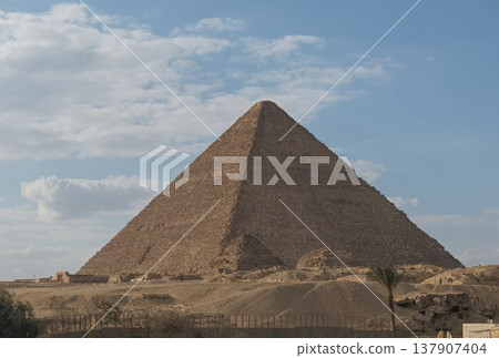 The Great Pyramid of Giza stands tall beneath the blue sky and clouds. The Great Pyramid of Giza stands tall beneath the blue sky and clouds. 137907404