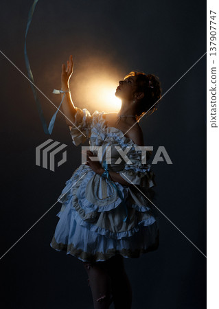 Young woman in ornate Rococo dress reaching toward glowing star in dark studio 137907747