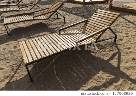 empty wooden sun beds on the sandy beach after the end of the season, empty sun beds on the beach at the beginning of autumn in Europe in cold weather 137908929