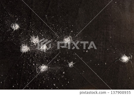 thin broken glass on black paper, dents and dots on the glass where it broke, white cracks and completely broken places on the glass on a black uneven background 137908935