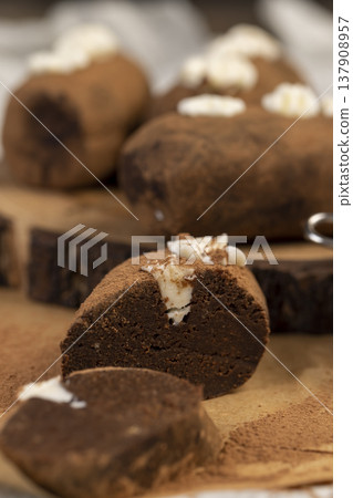sweet brown pastry potatoes are lying on a serving board and paper, sweet classic cake from butter and cocoa mixed with sponge cake and cognac, cocoa powder is scattered nearby 137908957