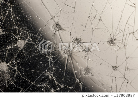 thin broken glass on black paper, dents and dots on the glass where it broke, white cracks and completely broken places on the glass on a uneven background 137908987