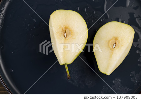 sliced ripe pears on a blue ceramic bowl on the table, several ripe hard and juicy pears are lying on a bowl on the kitchen table, the pears are covered with water and split into halves 137909005