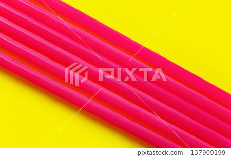 Six pink plastic drinking straws on yellow board, forming diagonal line - abstract closeup detail 137909199