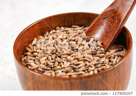 Blessed milk thistle seeds - Silybum marianum - in small wooden cup with spoon on white stone like board, 137909207