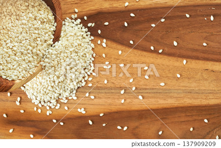 White sesame seeds pouring from small cup to wooden table, view from above White sesame seeds pouring from small cup to wooden table, view from above 137909209
