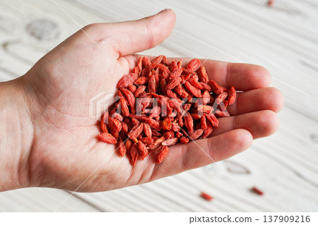 Young man hand with dried goji berries over white boards desk, closeup detail Young man hand with dried goji berries over white boards desk, closeup detail 137909216