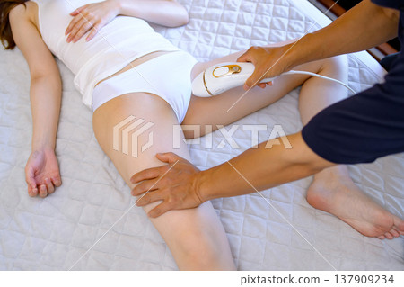 Women getting help with VIO hair removal from their partners (boyfriends, husbands) using home hair removal devices. Women getting help with VIO hair removal from their partners (boyfriends, husbands) using home hair removal devices. 137909234