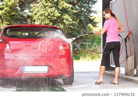 Young woman washing her red car in self serve carwash, view from back Young woman washing her red car in self serve carwash, view from back 137909238