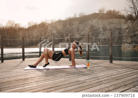Beautiful Woman Performing Bridge Yoga Pose Outdoors At Lake. Glutes And Core Strength Training Concept Beautiful Woman Performing Bridge Yoga Pose Outdoors At Lake. Glutes And Core Strength Training Concept 137909718