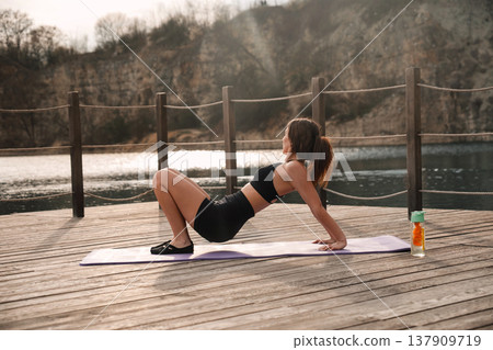 Pretty Woman Holding Bridge Yoga Pose On Mat At Lake. Outdoor Fitness And Core Stability Concept Pretty Woman Holding Bridge Yoga Pose On Mat At Lake. Outdoor Fitness And Core Stability Concept 137909719
