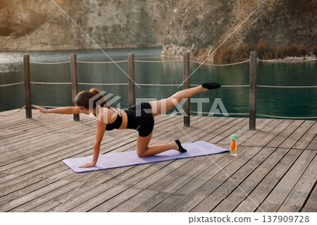 Pretty Woman Performing Bird Dog Exercise On Yoga Mat At Lake. Core Stability And Balance Training Concept Pretty Woman Performing Bird Dog Exercise On Yoga Mat At Lake. Core Stability And Balance Training Concept 137909728
