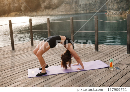 Attractive Woman Practicing Bridge Yoga Pose Outdoors At Lake. Glutes And Core Strength Training Concept Attractive Woman Practicing Bridge Yoga Pose Outdoors At Lake. Glutes And Core Strength Training Concept 137909731