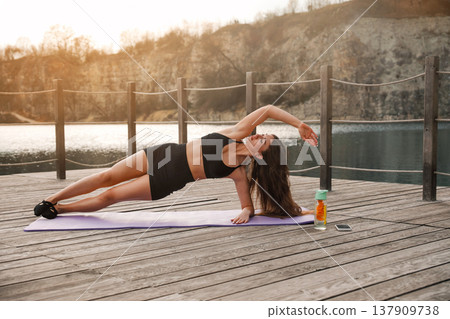 Attractive Woman Practicing Side Plank Variation Outdoors At Lake. Core Stability And Balance Training Concept Attractive Woman Practicing Side Plank Variation Outdoors At Lake. Core Stability And Balance Training Concept 137909738