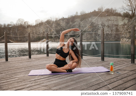 Young Woman Practicing Seated Yoga Stretch On Mat At Lake. Flexibility And Balance Training Concept 137909741