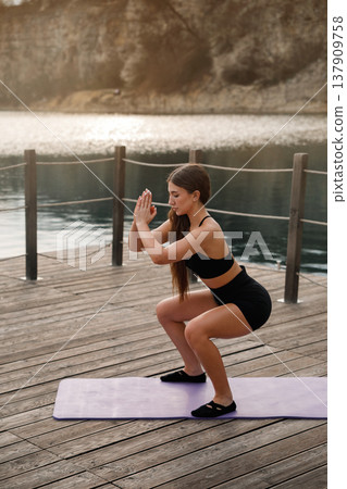 Fit Pretty Woman Holding Deep Squat On Yoga Mat At Lake. Lower Body Workout And Strength Training Outdoors Fit Pretty Woman Holding Deep Squat On Yoga Mat At Lake. Lower Body Workout And Strength Training Outdoors 137909758