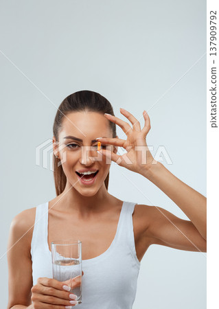 Portrait of beautiful woman holding glass of fresh water. Smiling girl taking omega 3 fish oil capsule, Portrait of beautiful woman holding glass of fresh water. Smiling girl taking omega 3 fish oil capsule, 137909792