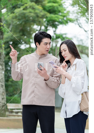 A couple looking at their smartphones outdoors. 137909843