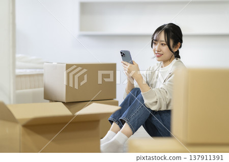 一位年輕女子坐在被紙箱包圍的地方,低頭看著她的智慧型手機。 (圖片來源:Moving) 一位年輕女子坐在被紙箱包圍的地方,低頭看著她的智慧型手機。 (圖片來源:Moving) 137911391