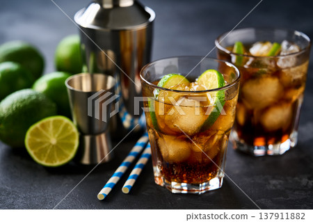 alcoholic cocktail Cuba Libre composed of rum, cola, ice cubes, lime on a dark table. alcoholic cocktail Cuba Libre composed of rum, cola, ice cubes, lime on a dark table. 137911882