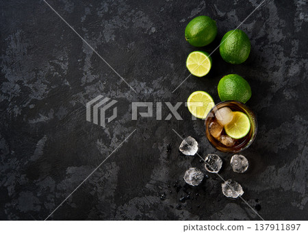 alcoholic cocktail Cuba Libre composed of rum, cola, ice cubes, lime on a dark table top view. 137911897