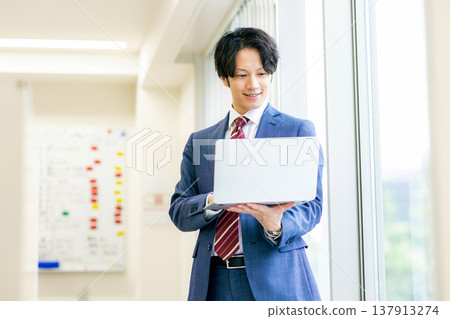 A young man smiles while operating his laptop. A young man smiles while operating his laptop. 137913274