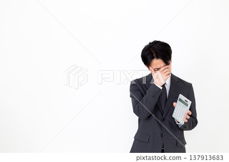 一位穿著西裝的中年男性商人拿著計算器，憂心忡忡 137913683
