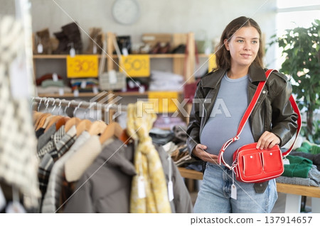 Pregnant woman choosing handbag in clothing store Pregnant woman choosing handbag in clothing store 137914657
