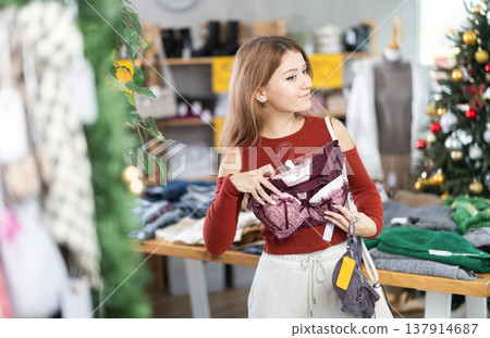 Girl client looks at products in store, looks closely at bra, picks up wardrobe item 137914687