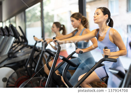 Sportive young girls doing air bike exercises in well-equipped gym 137914708