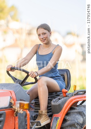 Young woman sits on minitractor and drives rural vehicle, performs loading work on farm 137914746