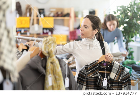 Middle-aged woman choosing winter coat in clothing store Middle-aged woman choosing winter coat in clothing store 137914777