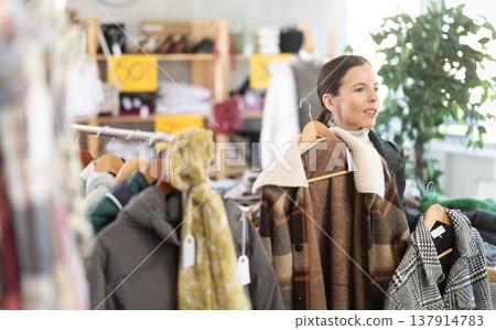Woman chooses checkered jacket searches for fashionable clothes in clothing boutique 137914783