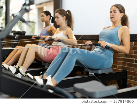 Sportive young girls training on cable row machine in gym Sportive young girls training on cable row machine in gym 137914800