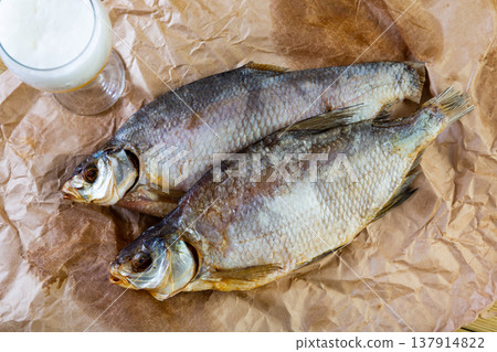 On table covered with paper is beer and snack - dried jerked bream, whole fish 137914822