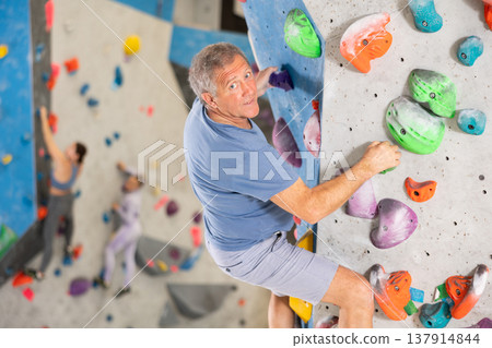 Alpinist practicing indoor rock climbing on artificial boulder without safety belts Alpinist practicing indoor rock climbing on artificial boulder without safety belts 137914844