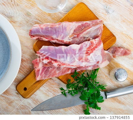 Slabs of raw pork ribs and fresh greens on wooden cutting board Slabs of raw pork ribs and fresh greens on wooden cutting board 137914855
