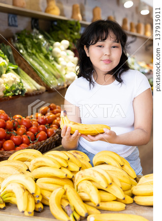 Young girl choosing fresh bananas in fruit and vegetable section of supermarket Young girl choosing fresh bananas in fruit and vegetable section of supermarket 137915011