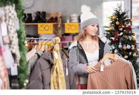 Young woman in hat choosing a sweater on Christmas tree background Young woman in hat choosing a sweater on Christmas tree background 137915014