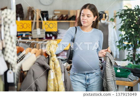 Pregnant woman choosing winter coat in clothing store Pregnant woman choosing winter coat in clothing store 137915049