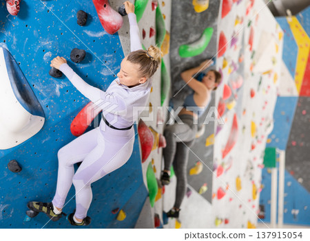 Young woman exercising on wall in climbing gym during bouldering training 137915054