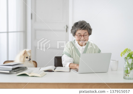 一位老婦人在辦公桌前工作,她心愛的博美犬陪伴在側。 一位老婦人在辦公桌前工作,她心愛的博美犬陪伴在側。 137915057