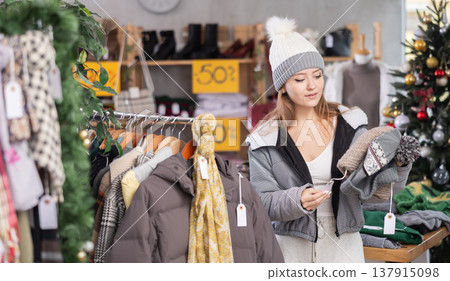 Girl client looks at products in store, looks closely at hat, picks up wardrobe item Girl client looks at products in store, looks closely at hat, picks up wardrobe item 137915098