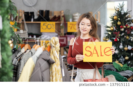 Girl with poster in hands announce mega Black Friday discounts in womens clothing store. Girl with poster in hands announce mega Black Friday discounts in womens clothing store. 137915111