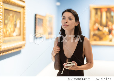 Woman visiting museum and looking at paintings in gold frames 137915167