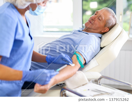 Old man having vein injection lying on clinical chair Old man having vein injection lying on clinical chair 137915262