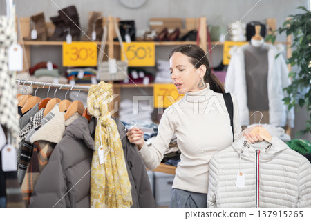Middle-aged woman choosing down jacket in clothing store Middle-aged woman choosing down jacket in clothing store 137915265