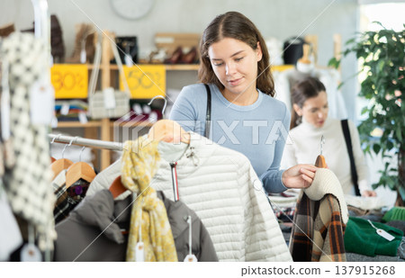Happy girl chooses fashionable down jacket in clothing store Happy girl chooses fashionable down jacket in clothing store 137915268