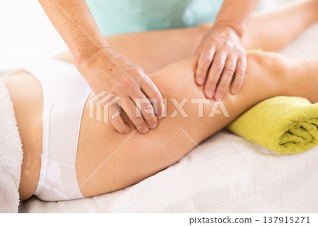 Hands of old masseur conducting hip massage for woman client Hands of old masseur conducting hip massage for woman client 137915271